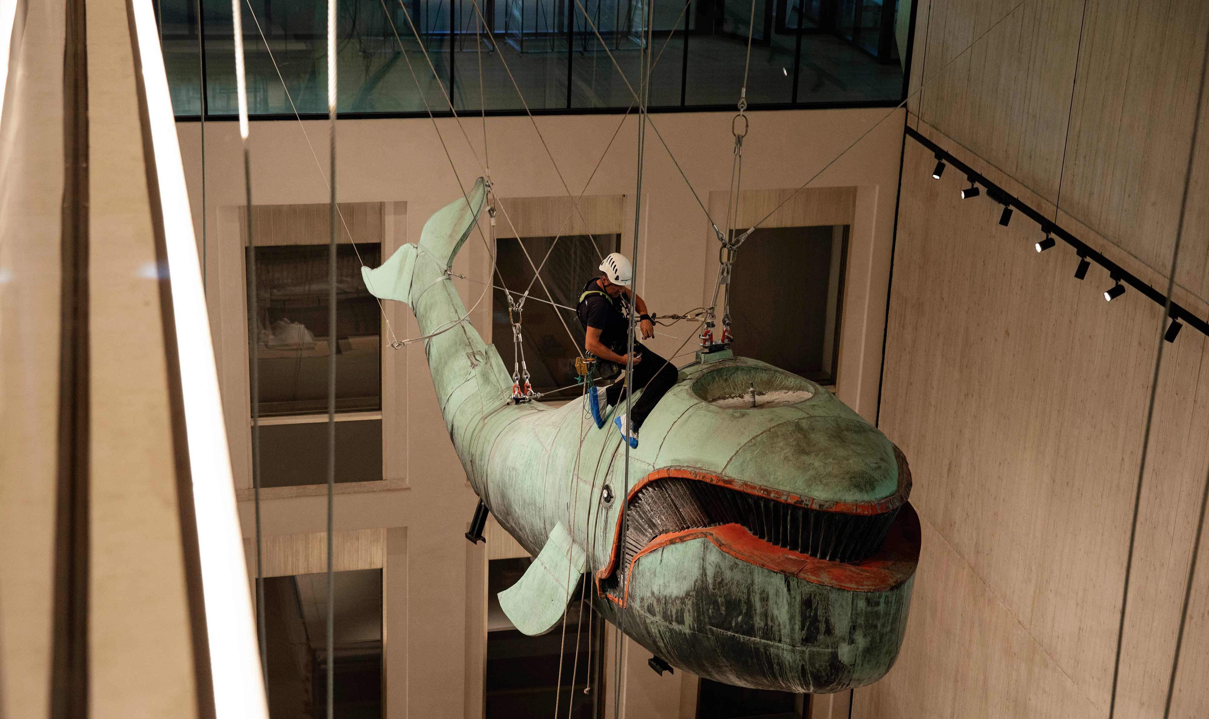 Mitarbeiter sitzt auf dem Rücken der in der Luft schwebenden Skulptur.