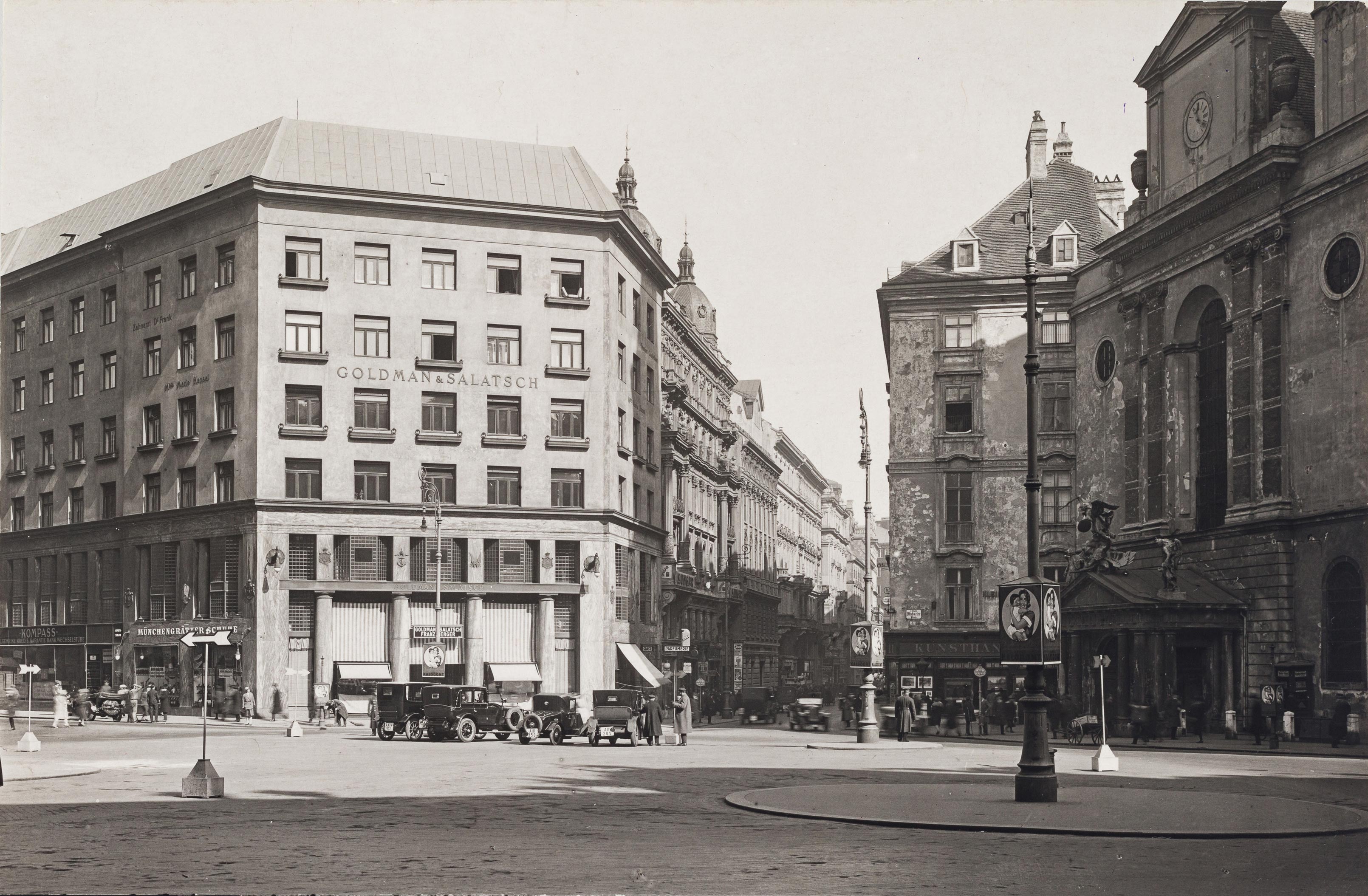 Schwarz-Weiß-Fotografie: Loos-Haus mit umliegenden Gebäuden, Autos und Personen