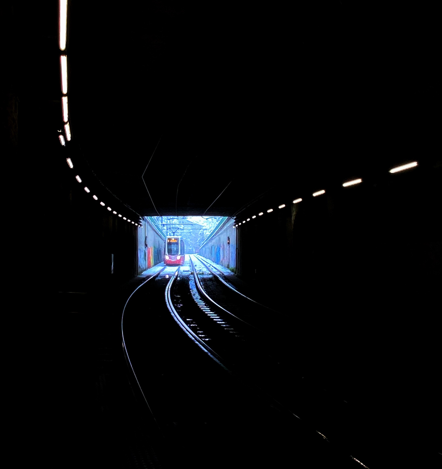 Eine Straßenbahn fährt von einer hellen Außenansicht in einen dunklen Tunnel.