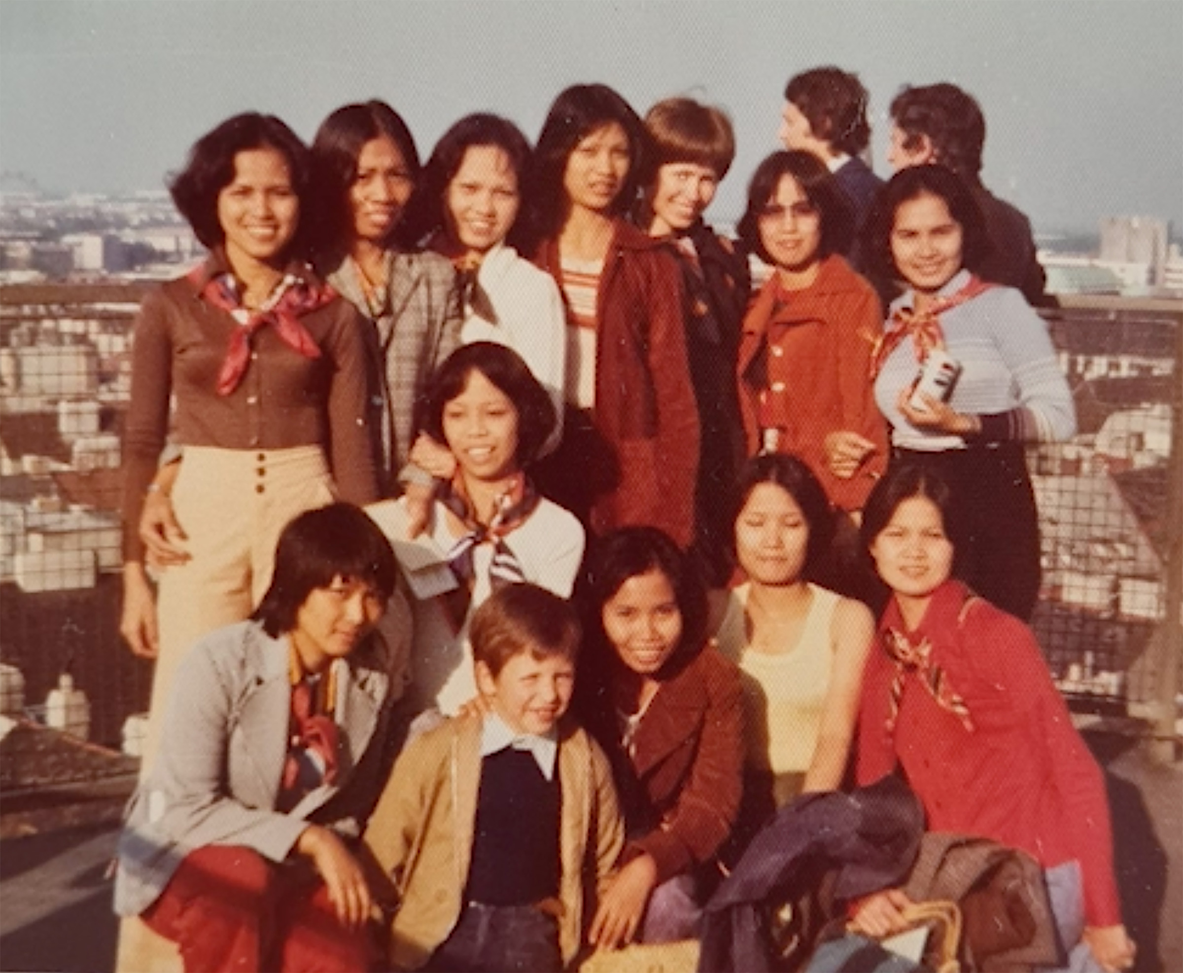 Eine Gruppe von Frauen und ein Kind posieren gemeinsam auf einem Dach mit Blick über eine Stadtlandschaft im Hintergrund.