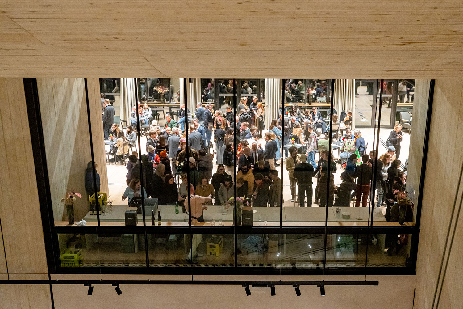 Blick vom 4. Stock durch ein Fenster in das Cafe im dritten Stock mit vielen Besucher:innen